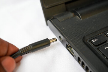 Man's hand plugging in connecting a power supply adapter cord plug into a generic laptop computer...