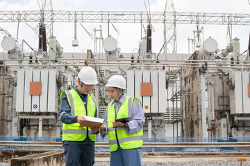 Power substation staff engineer work discussing plan in safety vest and helmet at electrical...