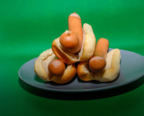 A unique arrangement of hot dogs and buns is presented on a blue plate, showcasing a playful and artistic display. The vibrant green backdrop enhances the composition