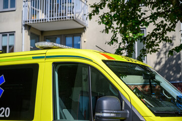 An emergency medical vehicle is parked near a residential building. The bright yellow design of the vehicle stands out against the backdrop of the modern architecture