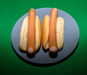 Two hot dogs placed in soft buns sit on a round gray plate. The vibrant green background adds a lively touch, perfect for a casual meal or gathering at home