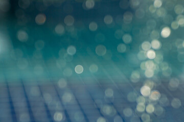 Abstract blue bokeh background of sunlight hitting water drops falling in a pool with blue tiled floor. Concept of nature background.