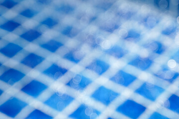 Abstract blue bokeh background of sunlight hitting water drops falling in a pool with blue tiled floor. Concept of nature background.