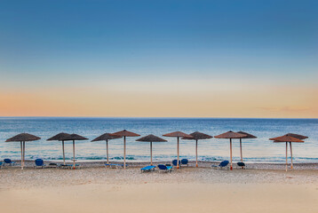 straw umbrella and sun loungers in line on a beach at sunset in Peloponnese Greece