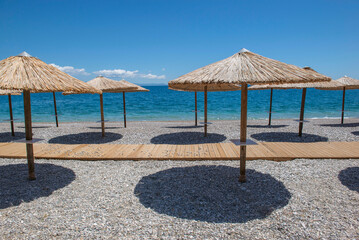straw umbrella on a beach iof pebbles n Peloponnese, Greece with their well drawn shadow in front beautiful sea