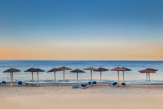 straw umbrella and sun loungers in line on a beach at sunset in Peloponnese Greece