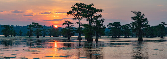 A colorful sunrise at beautiful Caddo Lake.  Bald cypress trees reflect in the calm water.