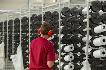 The worker controls the process. Factory equipment in perspective. Rows with coils of polypropylene threads for weaving cloth. Automatic machine.