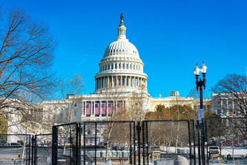 High fence in front of the Capitol building in Washington. Cityscape with blue sky.