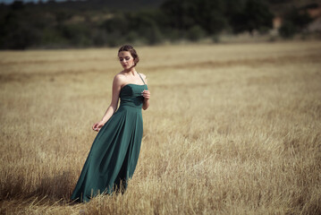 Elegant woman in green dress posing in golden wheat field