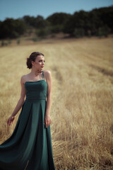 Elegant woman in green dress posing in golden wheat field