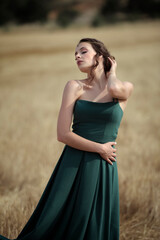 Elegant woman in green dress posing in golden wheat field