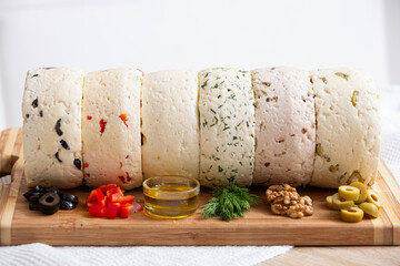 A variety of homemade cheese with different fillings of paprika, herbs, olives, olive oil and walnuts on a wooden board.