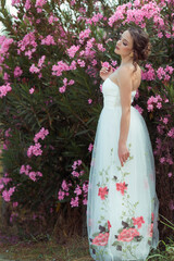 Elegant woman in embroidered white dress surrounded by pink oleander