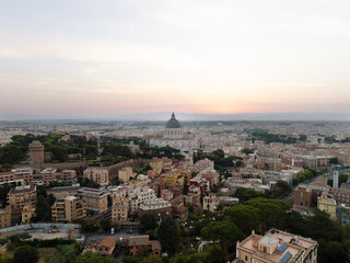 Peaceful cityscape of Rome at dusk, dominated by St. Peter’s Basilica’s towering dome, glowing against the warm and fading sunset sky. St. Peter’s Basilica silhouetted in evening light, its dome