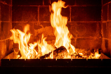 Interior fireplace glowing with fire, bright flames above stacked logs, cabin-like atmosphere, warmth concept, natural wood burning indoors