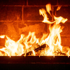 Interior fireplace glowing with fire, bright flames above stacked logs, cabin-like atmosphere, warmth concept, natural wood burning indoors