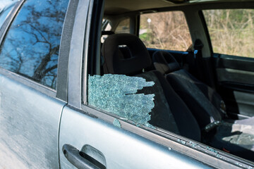 Realistic urban car crime image, broken glass remaining in window frame, vehicle left damaged, representing personal property theft, vulnerability on road