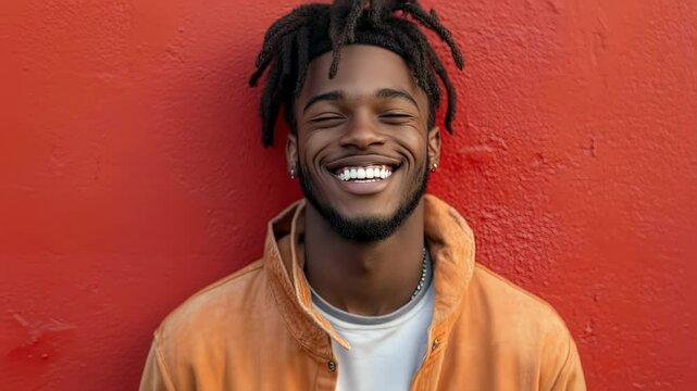 Portrait of a smiling young man with dreadlocks against a red wall