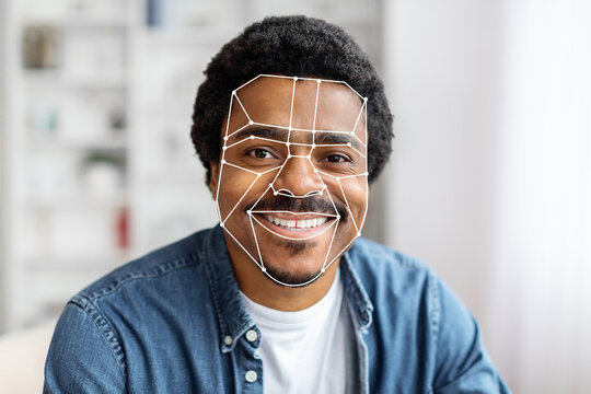 African American man is using facial recognition technology for identification at home. The digital overlay emphasizes facial features, showcasing advanced tech for seamless verification.