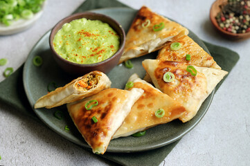 Homemade samosas on a plate filled with spicy mashed vegetables.