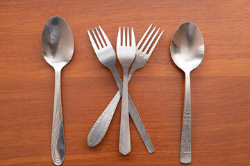 Still life of silverware shows spoons and forks on a brown wooden table surface