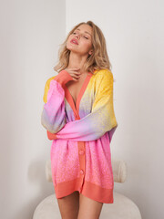 Beautiful blonde woman poses cheerfully in colorful cardigan at indoor setting
