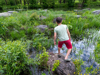 A young boy standing on a rock in the middle of a pond is preparing to bend