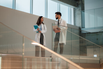Two doctors discussing on hospital stairs holding medical records
