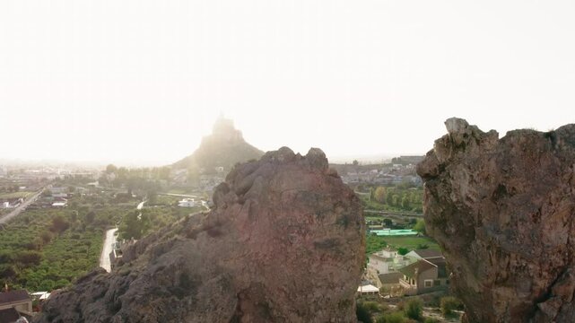 Monteagudo statue monument atop of rugged hill, overlooking cityscape during sunset. Ancient fortress and surrounding landscape. Culture and historical symbol. Murcia, Province of Alicante. Spain