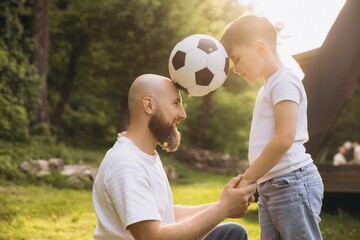 Obraz premium Father and son holding hands and playing with soccer ball celebrating father's day