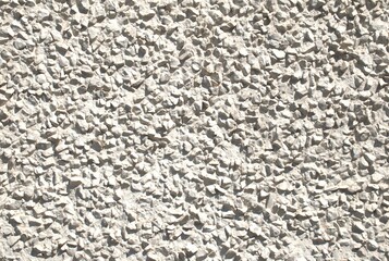 Close-up full-frame roughcast or pebble dash wall with a coarse, textured surface created by embedded small stones.  Rugged, light gray exterior. Cement, stucco, and aggregate. Urban outdoor wall.