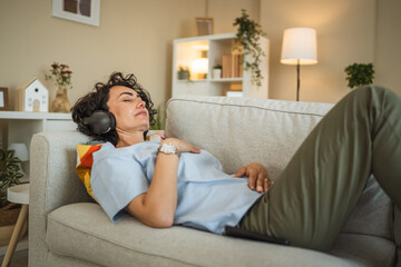 Mature woman lying on sofa with headphones and have guided meditation