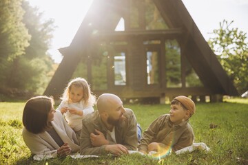 Family relaxing on grass in front of a frame cabin enjoying vacation