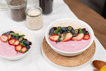Presented by fruits putting yogurt toppings with strawberry, berry, oats, raisins and chia seed decorated by peppermint in white blow. Pink background. Set of healthy dairy product choice. Pecuniary.