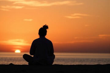 A silhouette of a woman sitting on the shore of a beach at sunset.