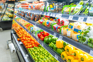 Supermarket vegetable refrigerated section with rows of packaged fresh produce including colorful bell peppers, tomatoes, limes and chili pepper. Freshness, convenience and healthy eating. Food retail