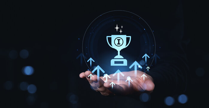 Hand holding glowing trophy icon with upward arrows representing success and achievement in futuristic digital style on dark background.