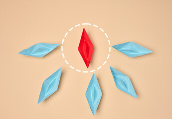 Leadership and individuality concept. One red origami boat surrounded by six blue boats on a beige...
