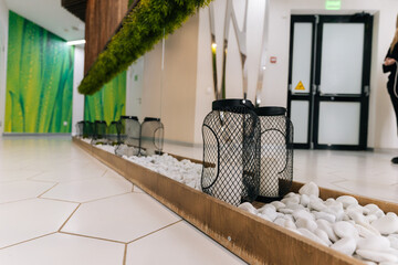 White pebbles and black wire lanterns decorating wooden tray in modern beauty clinic interior with...