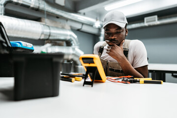 Young technician analyzes readings on a multimeter in a modern workshop during a training session