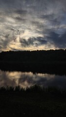 Fototapeta premium Scenic lakeside sunset view showing water reflections and dramatic sky, capturing natural light. Lakeside sunset, reflecting clouds create striking silhouette against horizon.