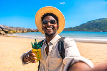 Smiling tourist enjoying tropical drink on beach takes selfie