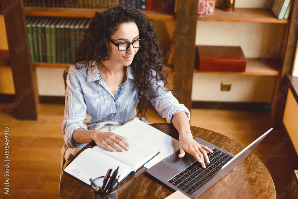 Poster above top high angle view of casual young woman in eyeglasses working on laptop, typing on keyboard,