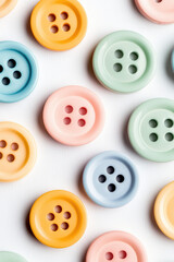 Colorful round buttons are scattered on a surface, each with four holes. Bright, playful arrangement with pastel hues
