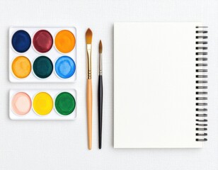Naklejka premium Watercolor paints, brushes, and blank sketchbook arranged on a light surface