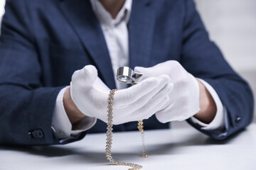 Appraiser evaluating luxury necklace at white table indoors, closeup