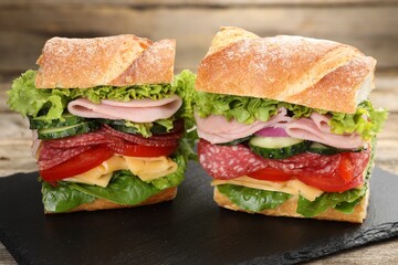 Tasty baguette sandwich with ham and vegetables on wooden table, closeup