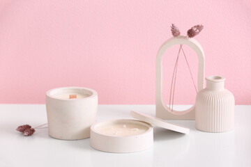 Holders with candles and decor on table near pink wall in room