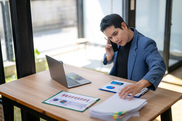 A man is talking on a cell phone while sitting at a desk with a laptop